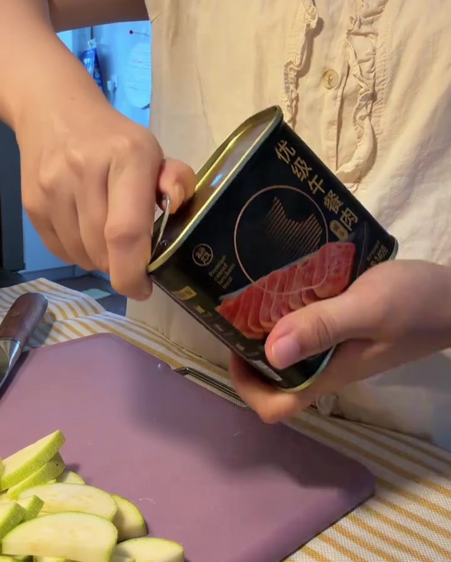 A block of luncheon meat being removed from its opened metal can.