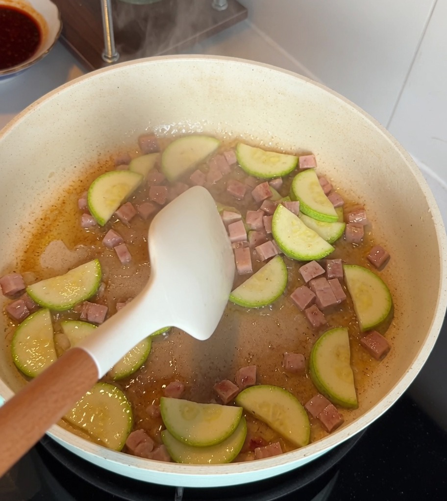 Zucchini slices and cubed luncheon meat stir-frying together in a non-stick pan.