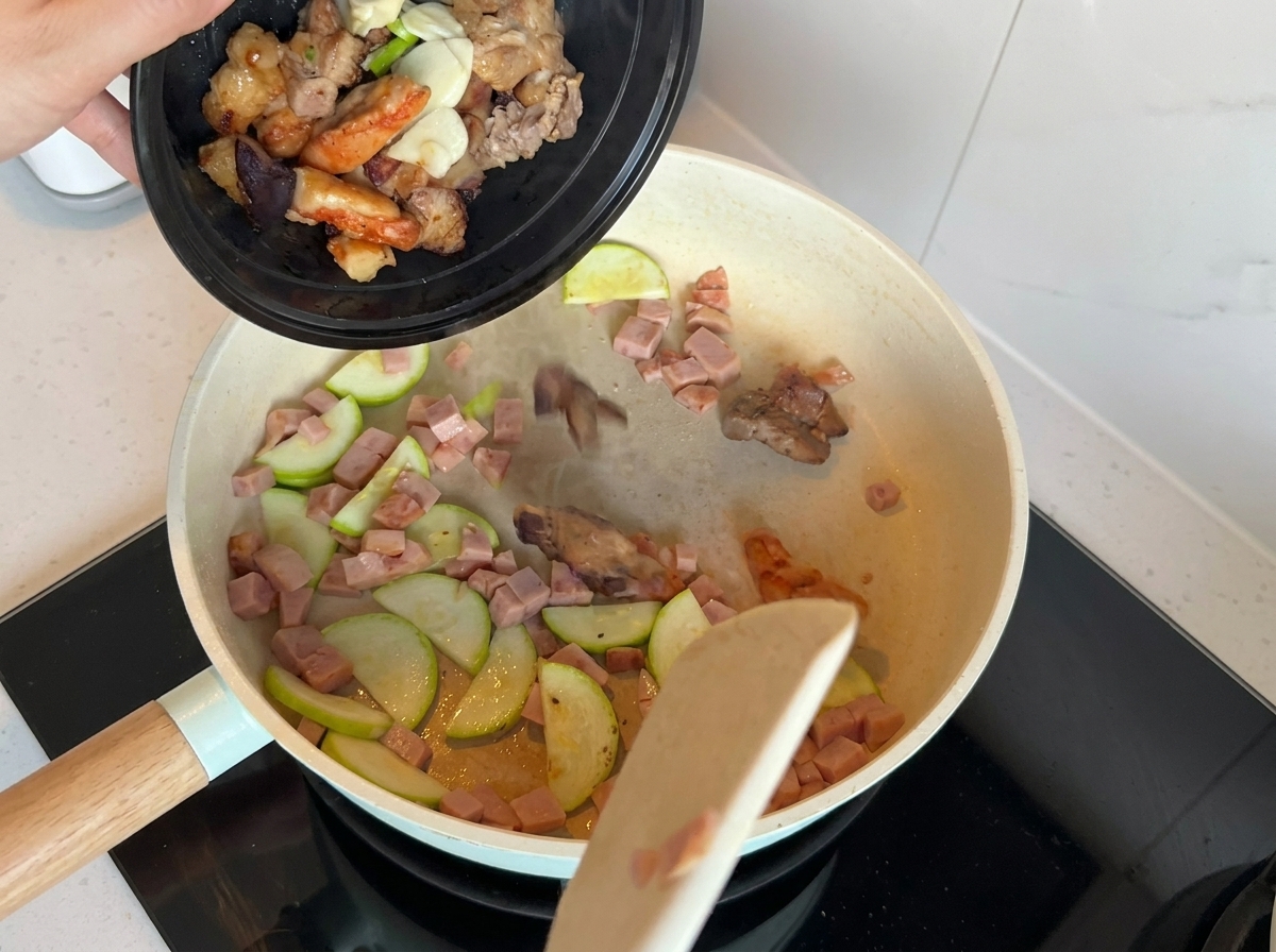 A pan containing stir-fried zucchini and luncheon meat with added scallions, garlic, and cooked meat pieces.