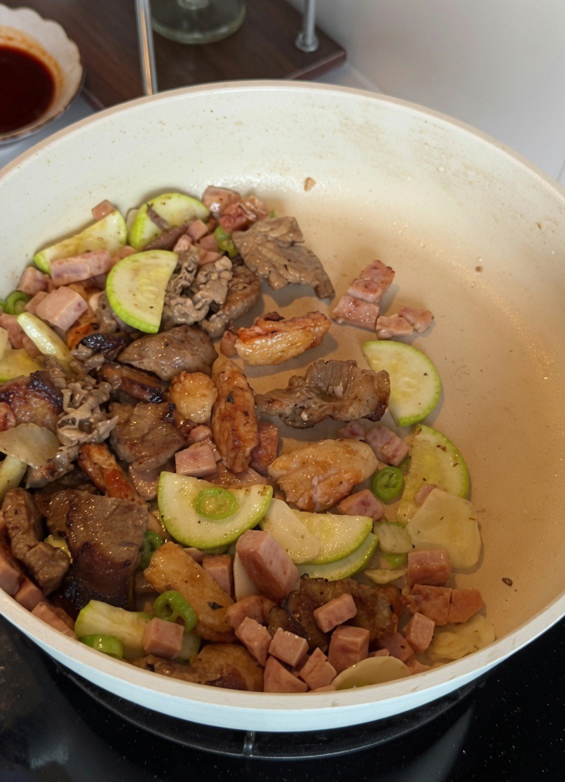 Beaten egg mixture being scrambled with zucchini and luncheon meat in a white pan.