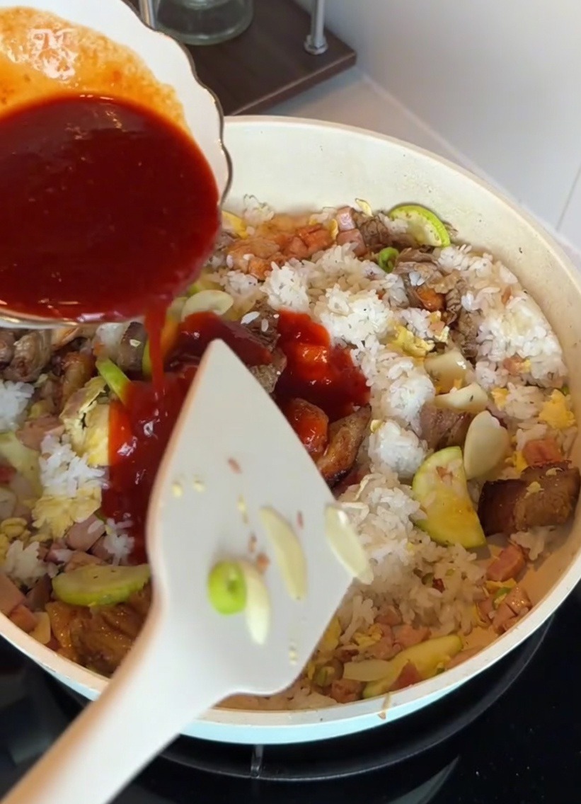 Korean-style bibimbap sauce being poured over rice and ingredients in a pan.