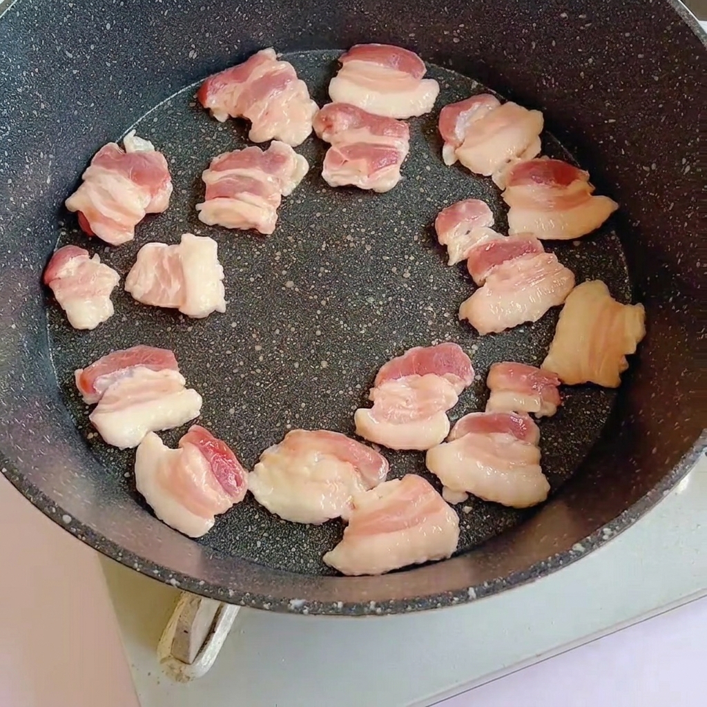 Slices of raw pork belly arranged in a hot pan, beginning to brown.
