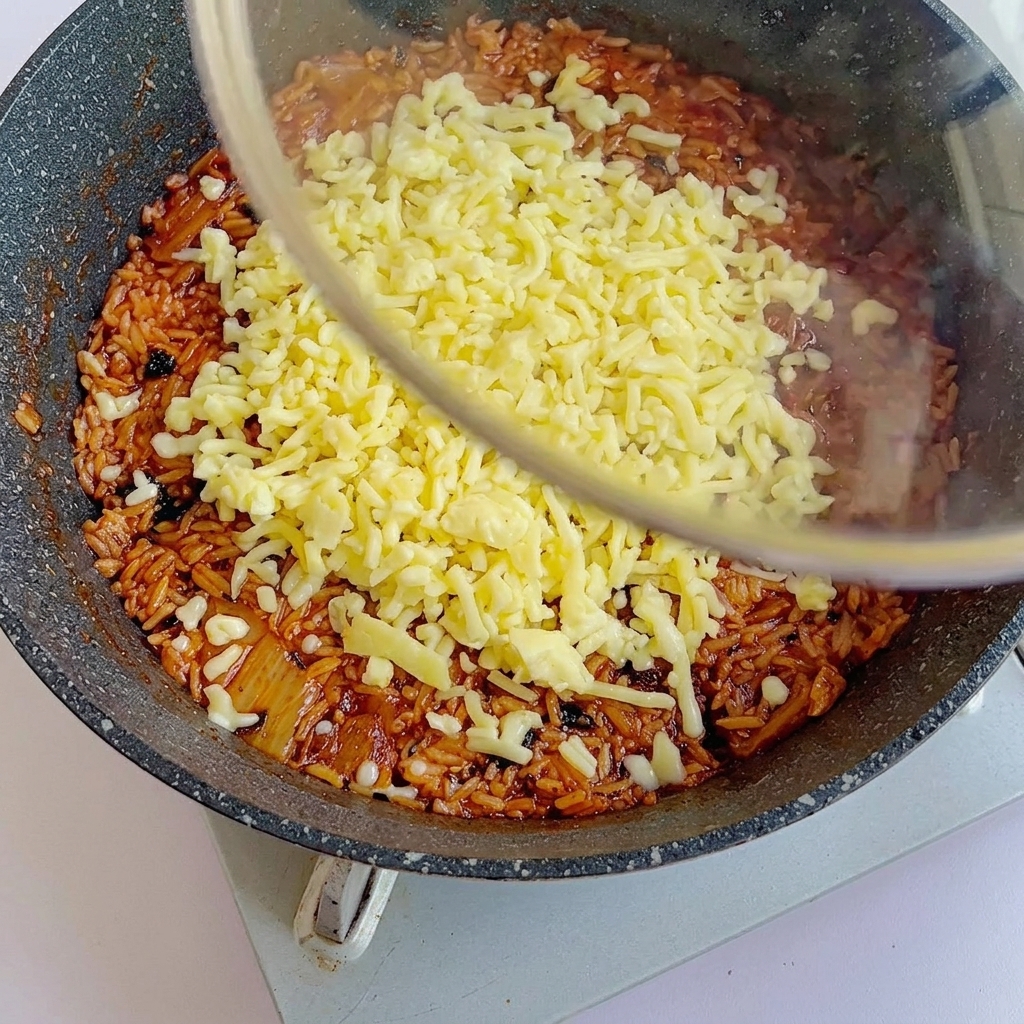 A glass lid being placed over the pan of cheesy fried rice to help the cheese melt.