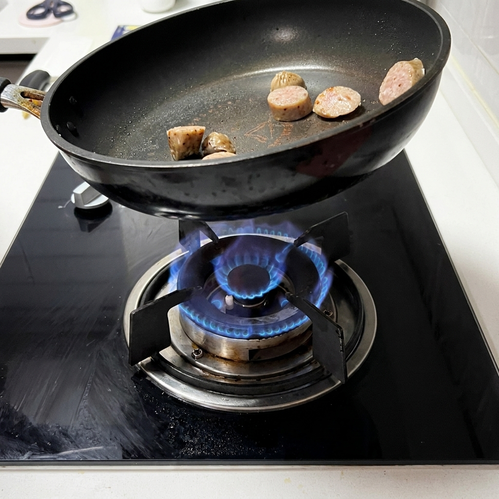 Slices of sausage sizzling and browning in a black pan on a gas stove.