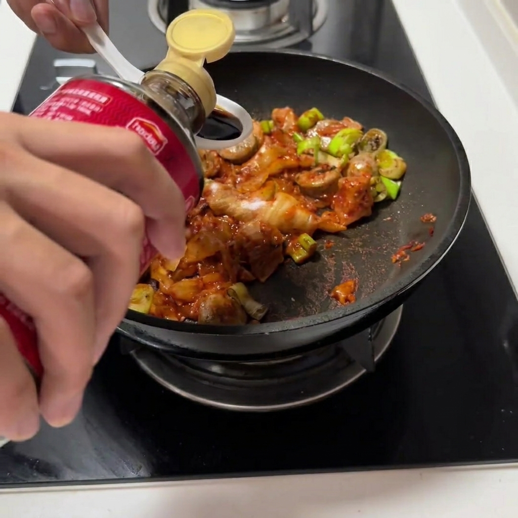 Soy sauce and oyster sauce being poured into the pan with the kimchi mixture.