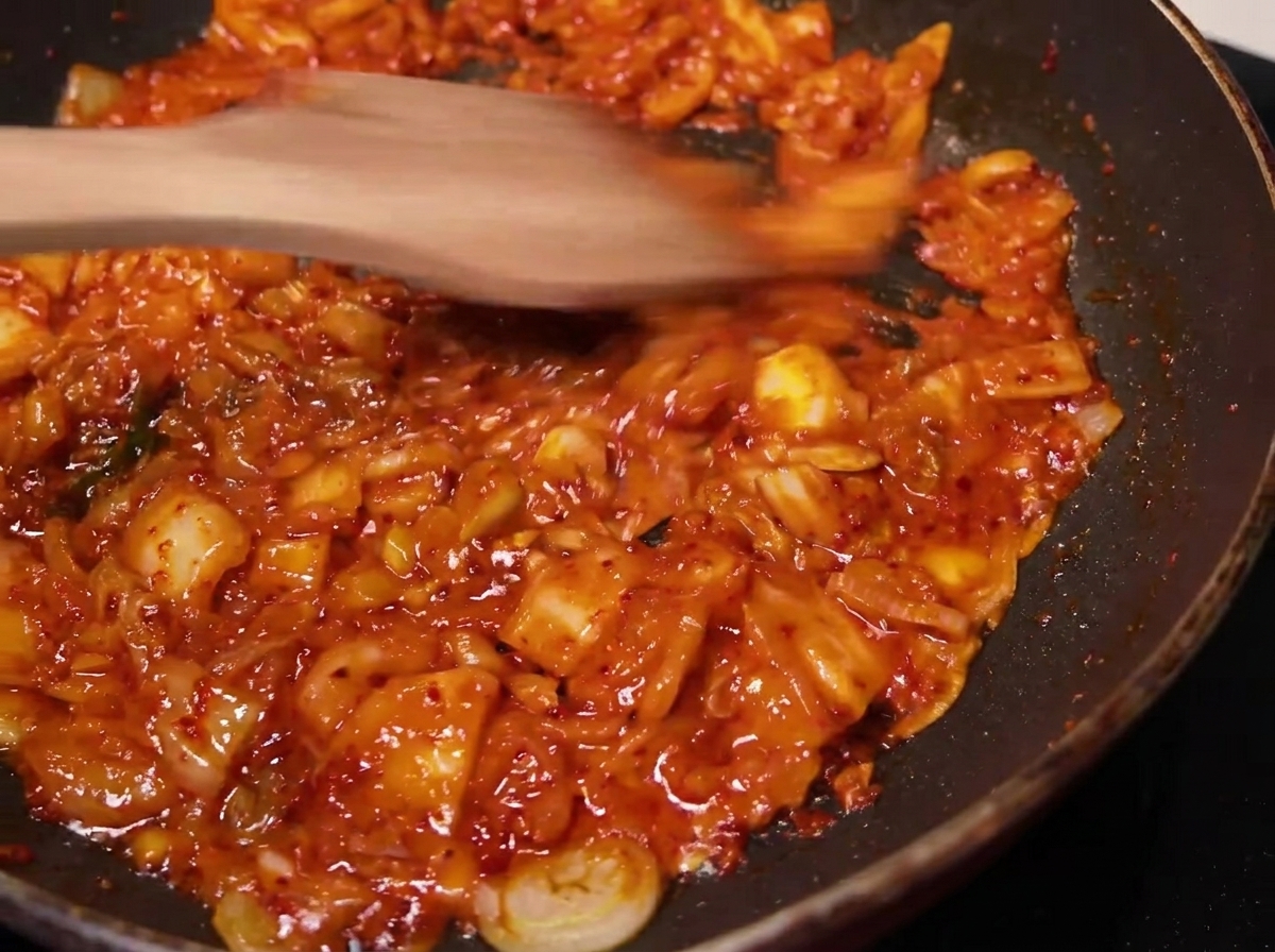 The seasoned kimchi mixture being stirred and cooked in a pan with a wooden spatula.