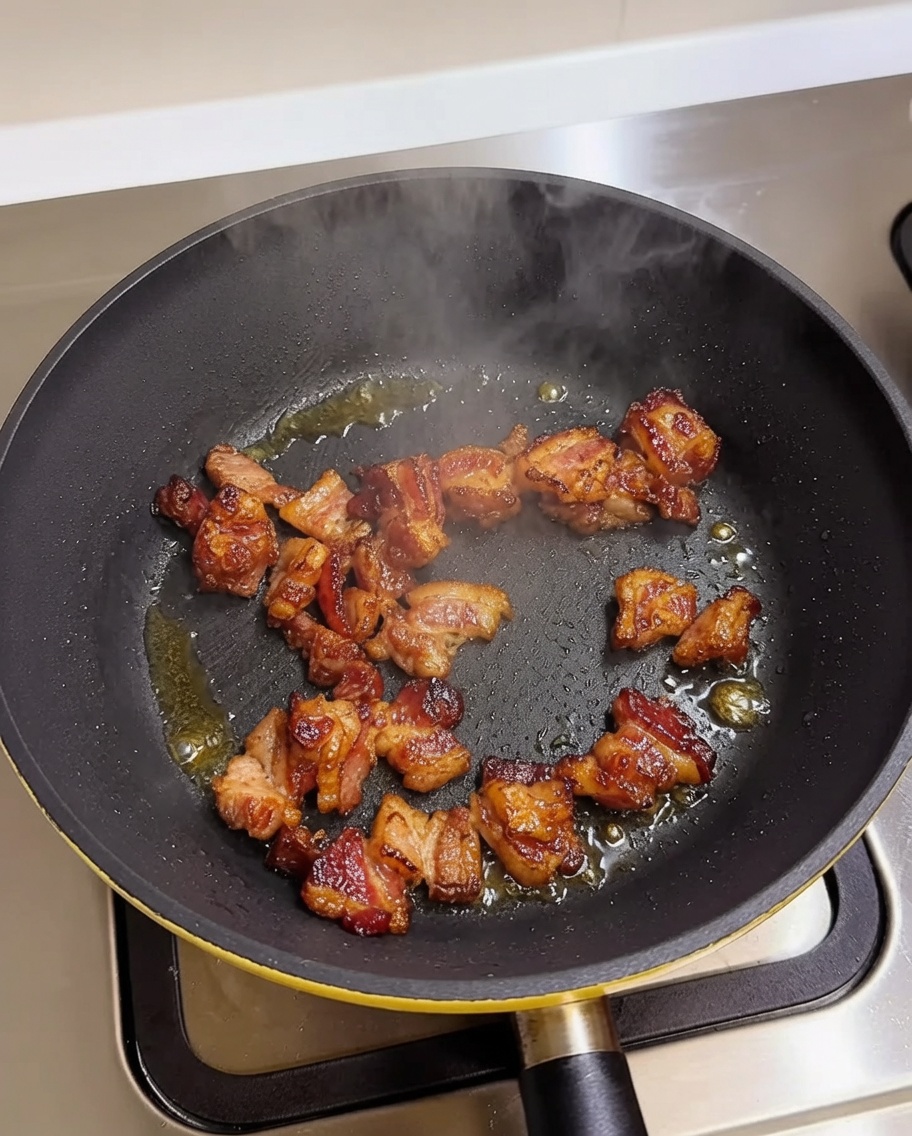 Pieces of pork belly browning in a hot frying pan.