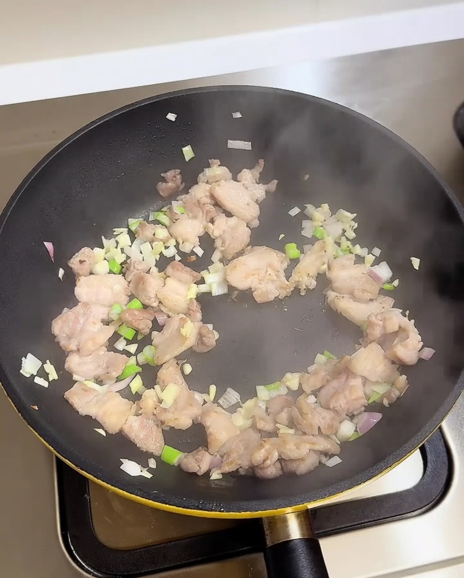Pork belly scallions garlic and onions being stir-fried in a pan with added seasoning liquids