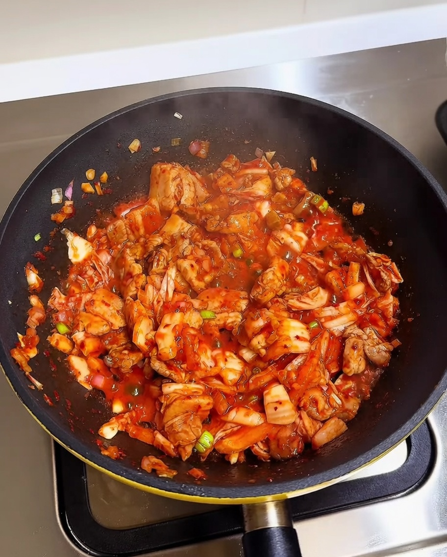 Cooked white rice being added to a pan containing stir-fried kimchi and pork belly.