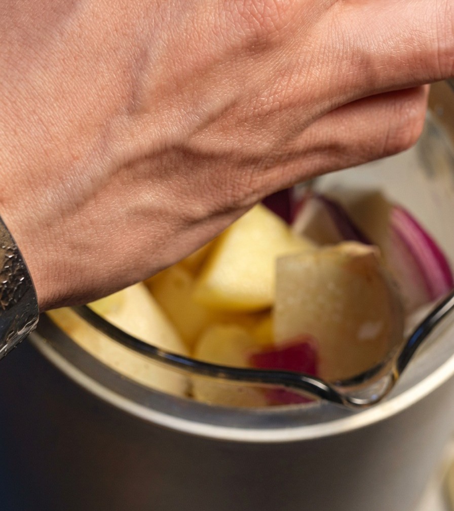 Red onion, apple, pear, and garlic pieces being added to a blender.