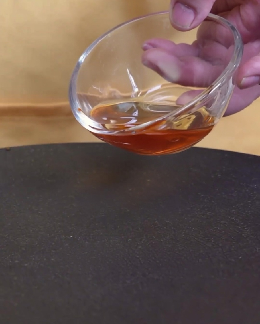 A close-up shot of sesame oil being poured from a glass bowl into a hot, empty pan.