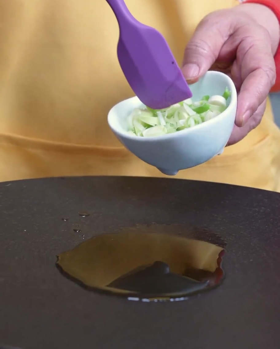 Green onions being stirred in a pan with sesame oil.