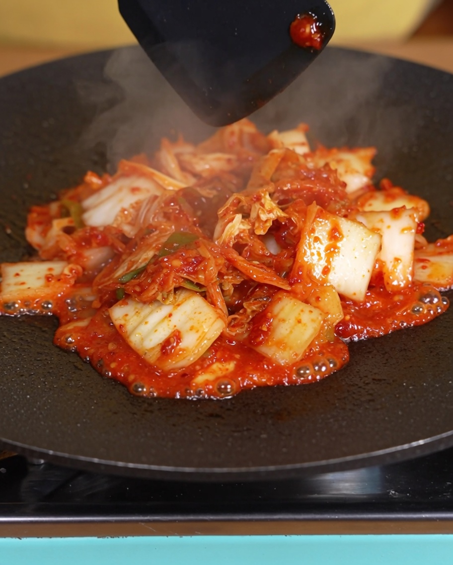 Kimchi being cooked in the pan with liquid visibly reduced.