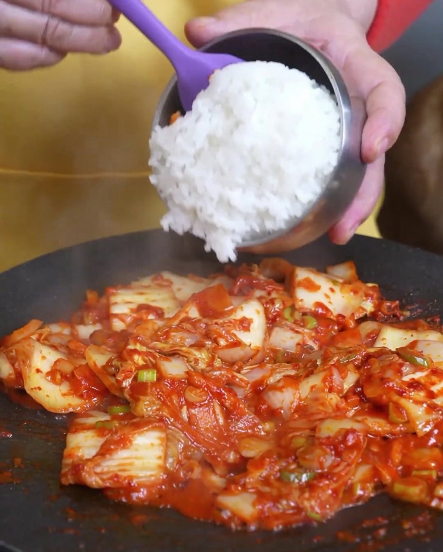 Cooked white rice being added to the pan containing the stir-fried kimchi.