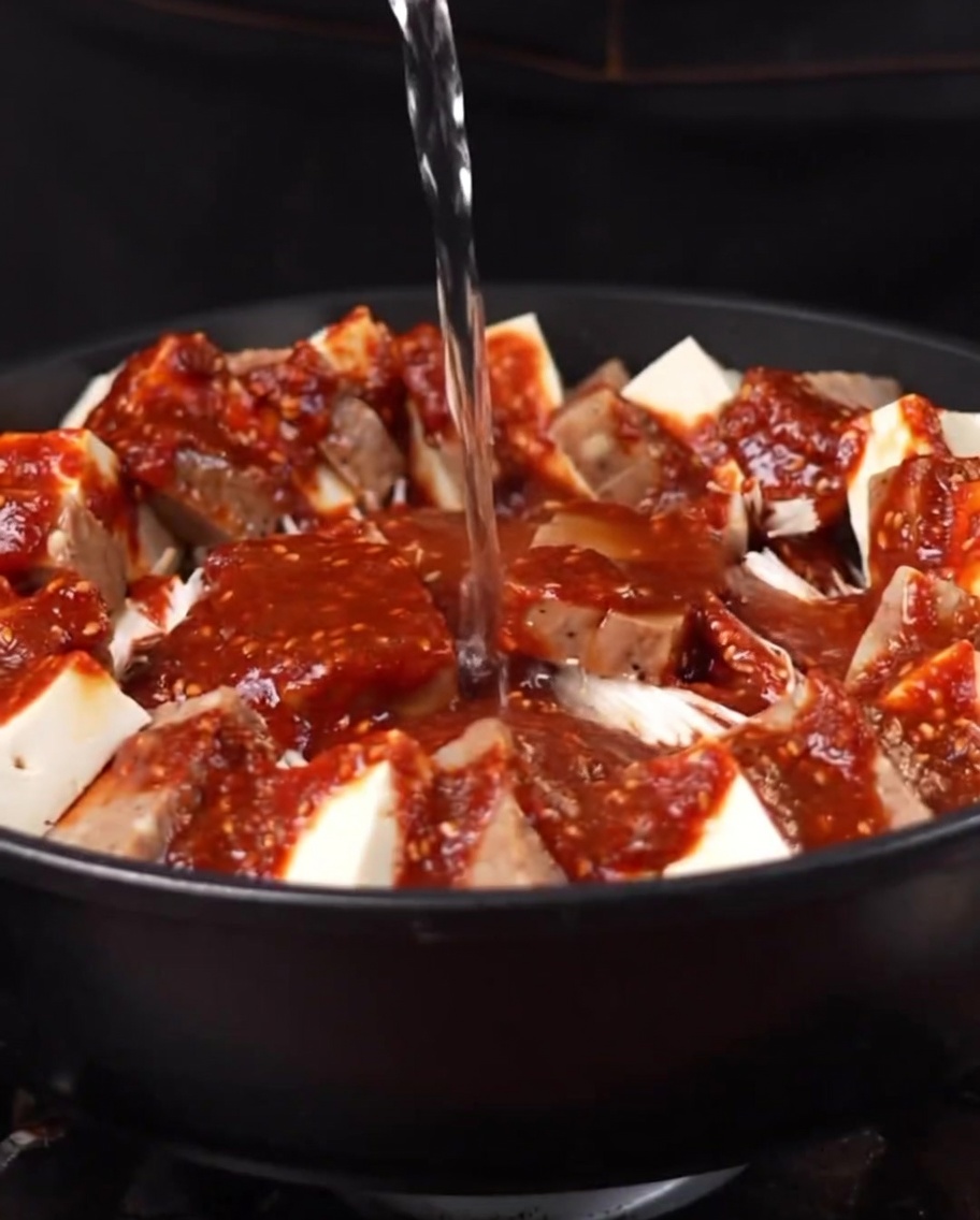 Boiling water being poured into the pot, starting to combine with the sauce and ingredients.