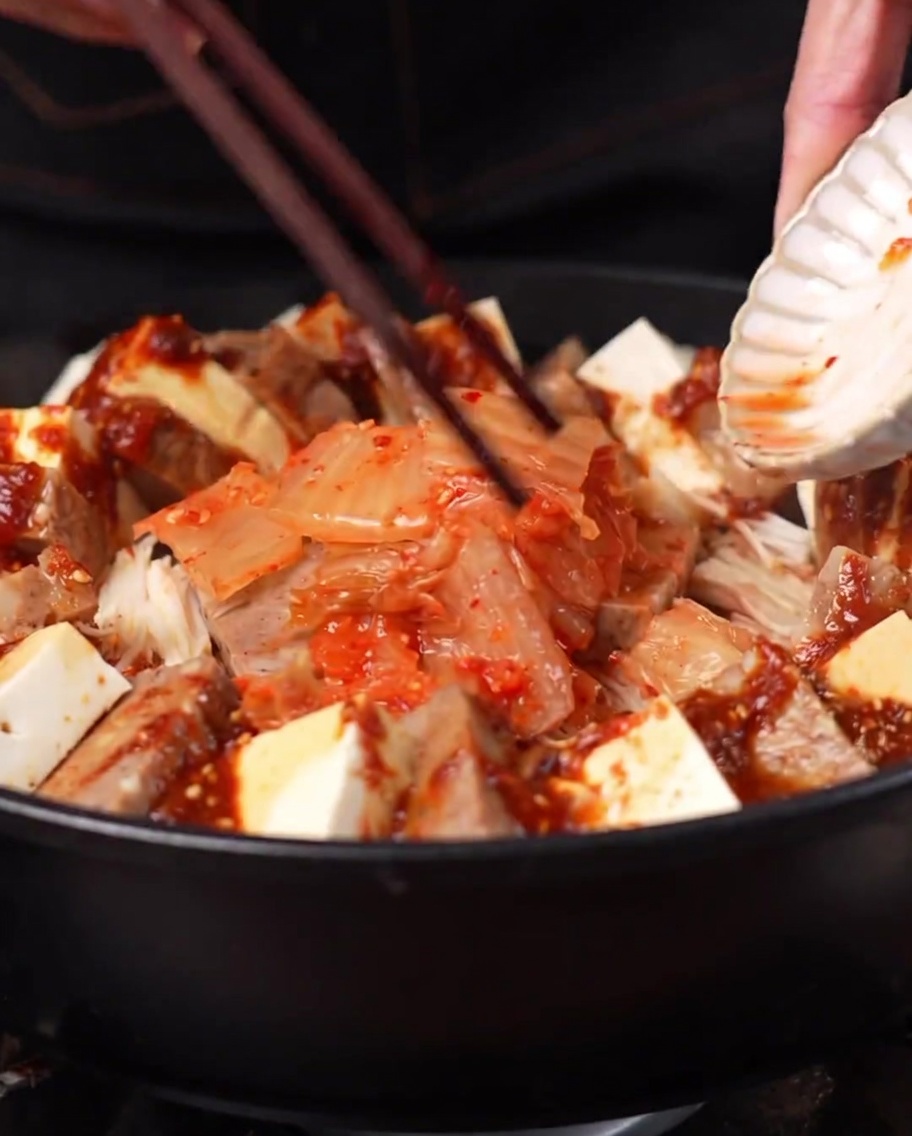 A mound of kimchi being added to the center of the pot surrounded by the other ingredients.