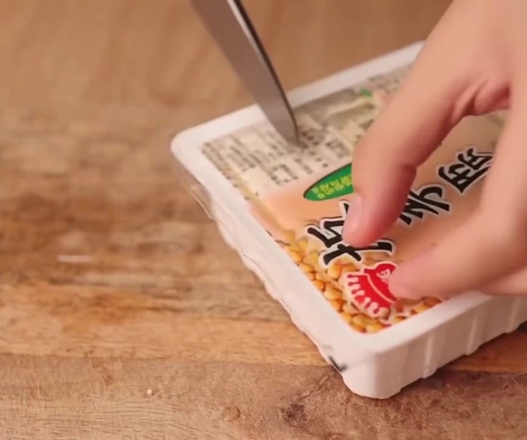 A block of firm tofu being cut into neat, uniform slices on a wooden board.