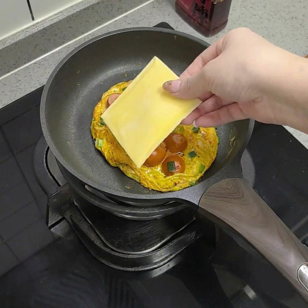 A slice of yellow cheese being placed onto the cooked egg and sausage mixture in the pan.