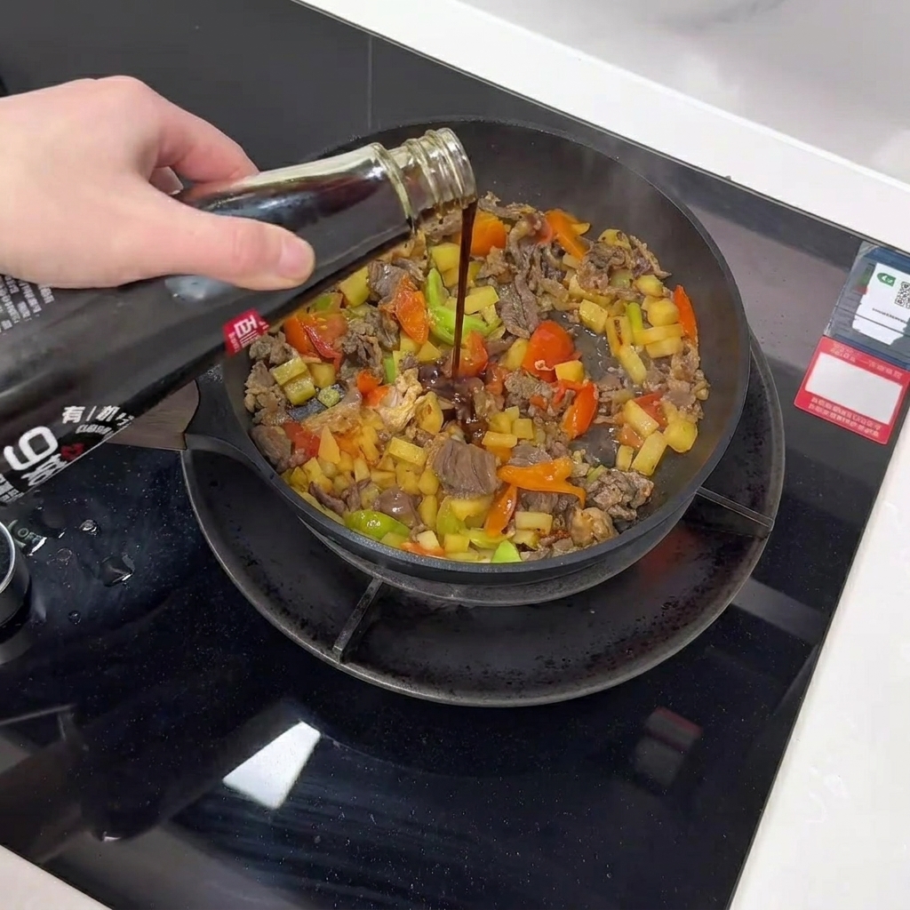 Dark mushroom sauce being poured from a bottle into a pan filled with beef, potatoes, and vegetables.