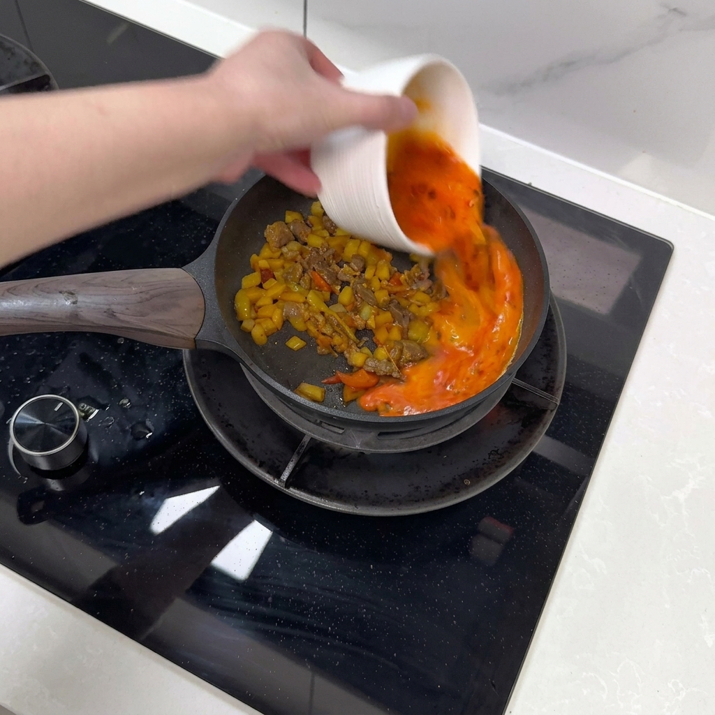 A beaten egg and chili mixture being poured into a pan over stir-fried ingredients.