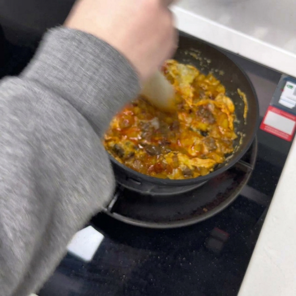A spatula dividing a cooking egg omelet into two halves inside a pan.
