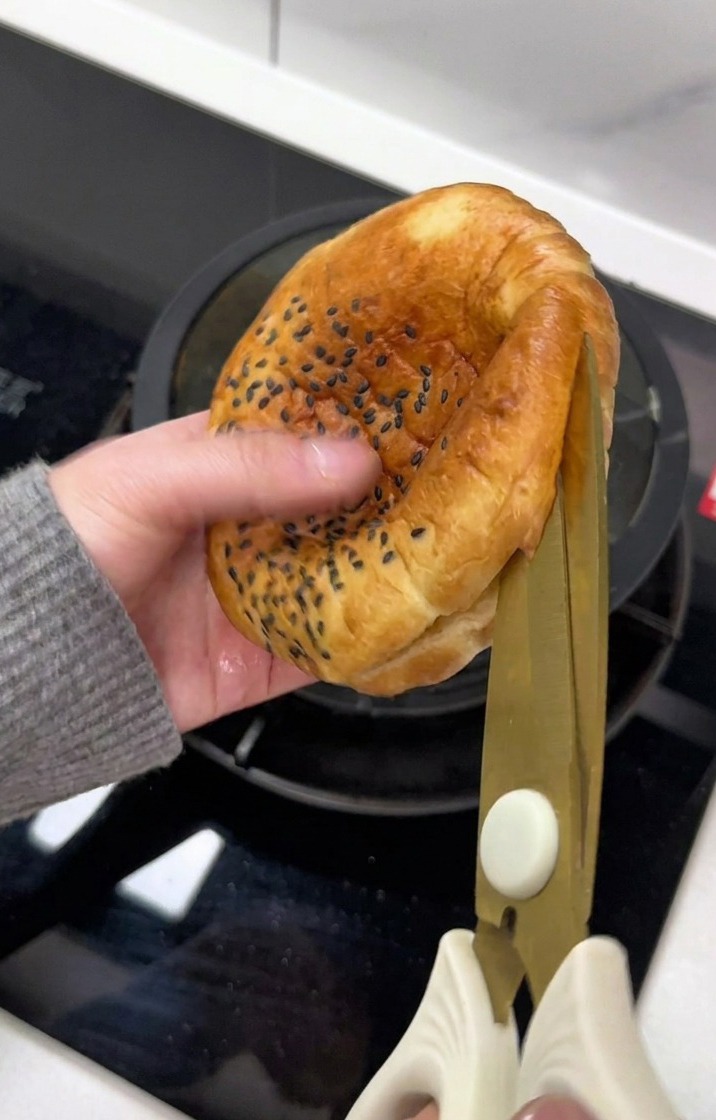 A hand using scissors to carefully slice open a toasted sesame seed burger bun.