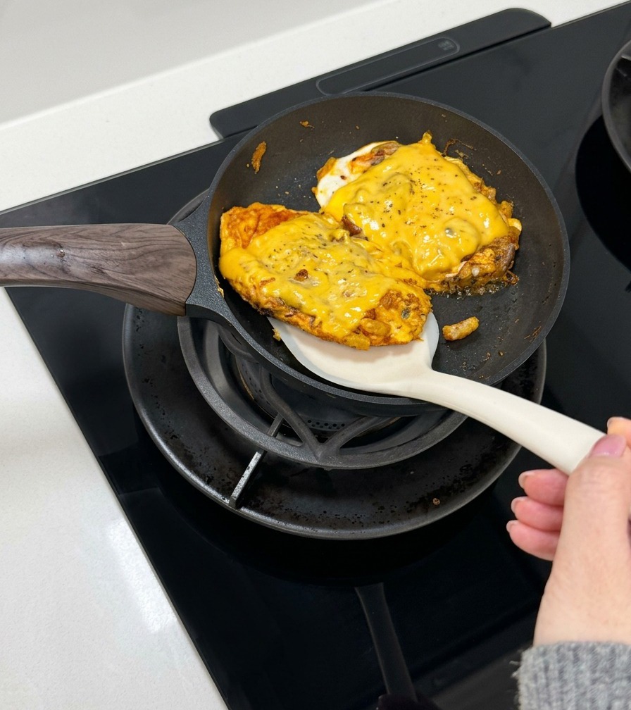 A spatula lifting a cooked, cheesy egg and beef patty to place it inside an opened burger bun.