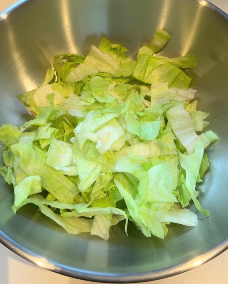 Shredded crisp lettuce placed in a large stainless steel mixing bowl.