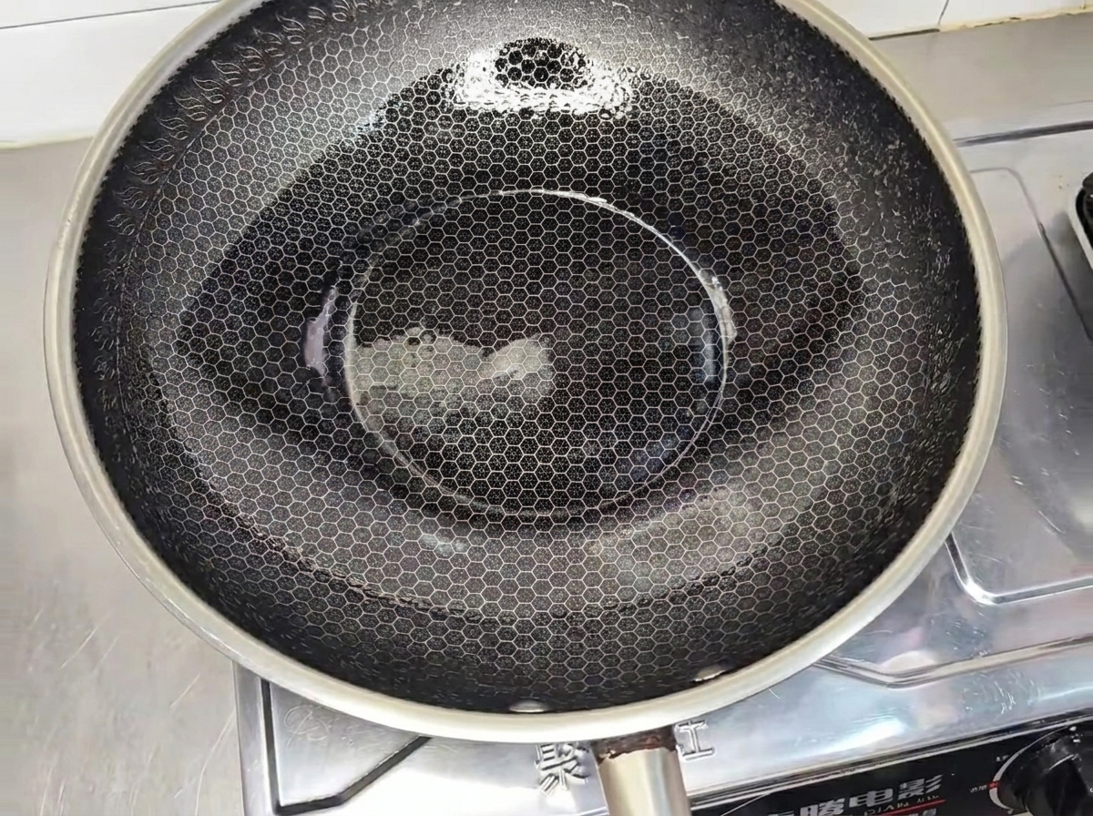 A seasoned chicken patty frying in a hot, oiled wok until golden brown.