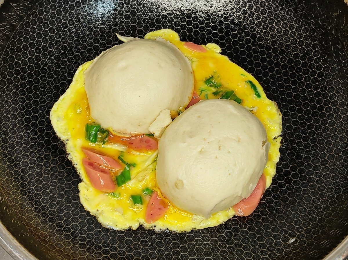 The flipped omelet with the cooked egg side facing up and the steamed buns underneath in a wok.