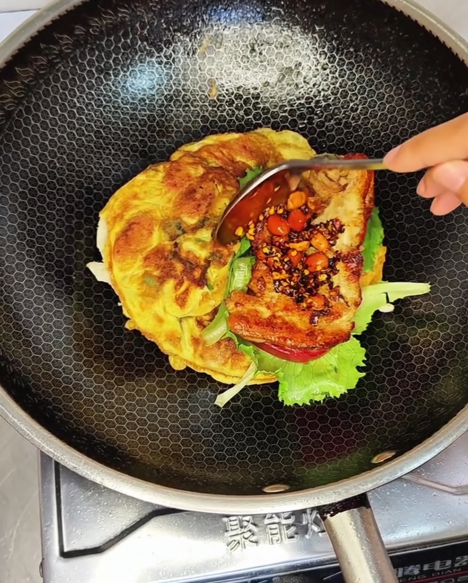 A fried chicken patty topped with a spoonful of chunky peanut chili sauce placed over lettuce in a wok.