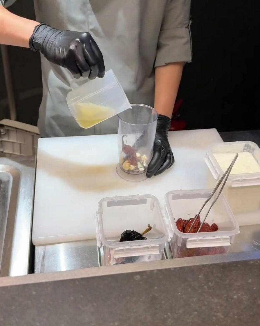 Immersion blender processing chili, egg yolk, and liquid in a container.