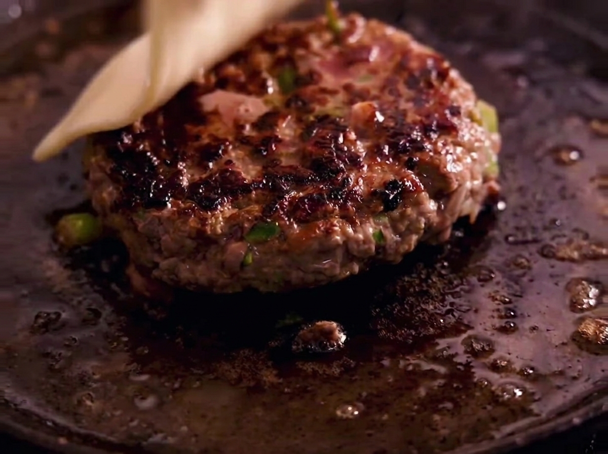 A slice of white cheese melting on top of a seared, juicy burger patty in a hot cast-iron skillet.