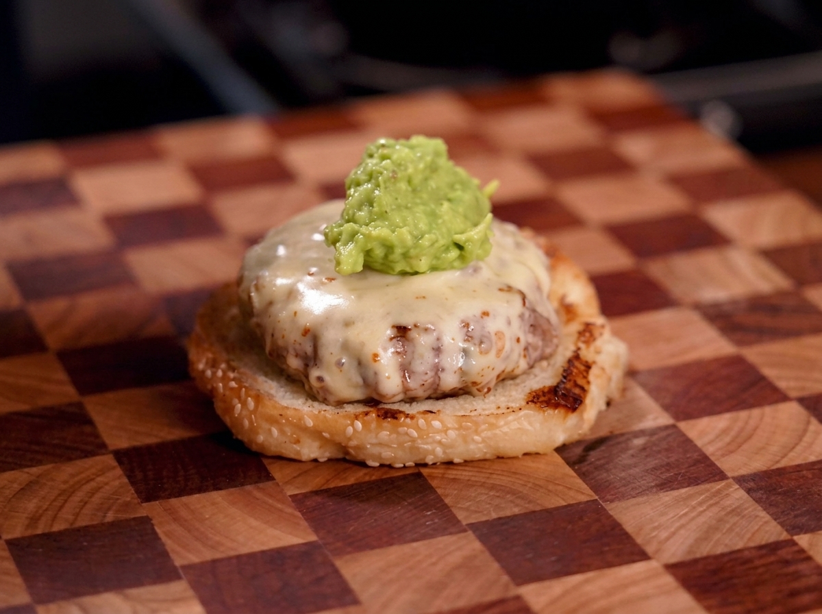 A dollop of chunky green guacamole sitting on top of a melted cheese-covered burger patty.
