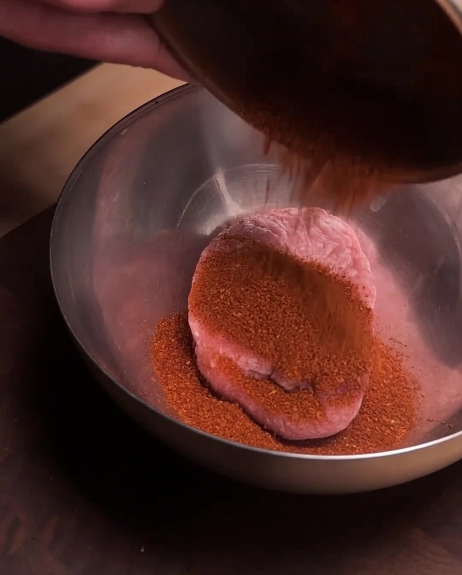 Fresh ground pork sitting in a stainless steel bowl with a layer of red spice powder poured over the top.