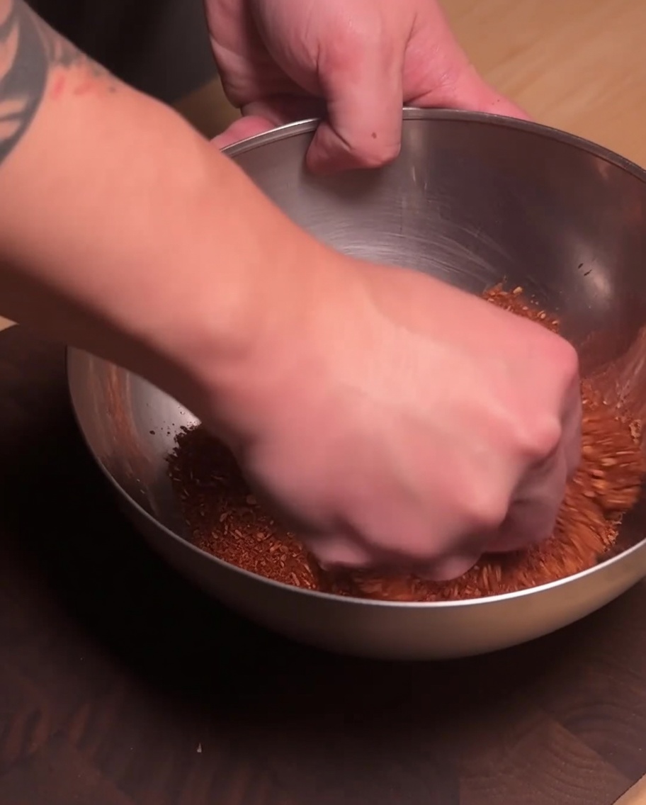 A hand mixing the seasoned ground pork and red spice powder together in a stainless steel bowl.