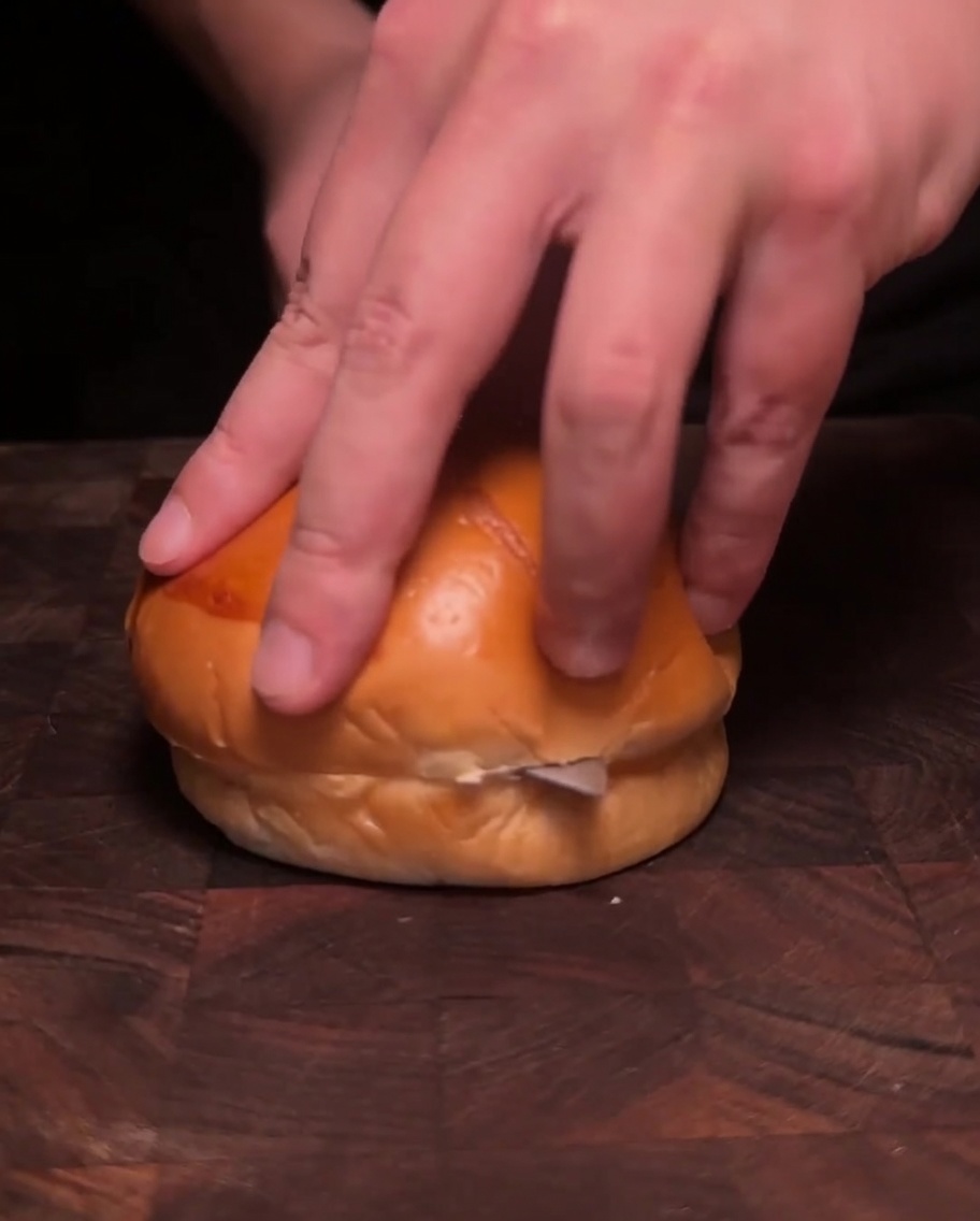 Two halves of a burger bun face down in a pan, toasting in melted butter until golden brown.