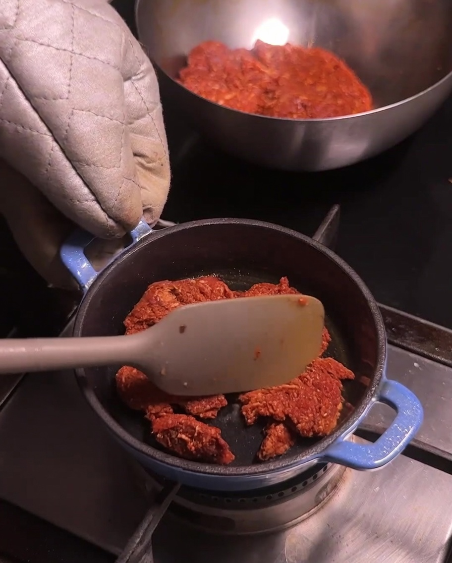 A small blue pot on a stovetop with crumbled chorizo pork being stirred with a light-colored spatula.
