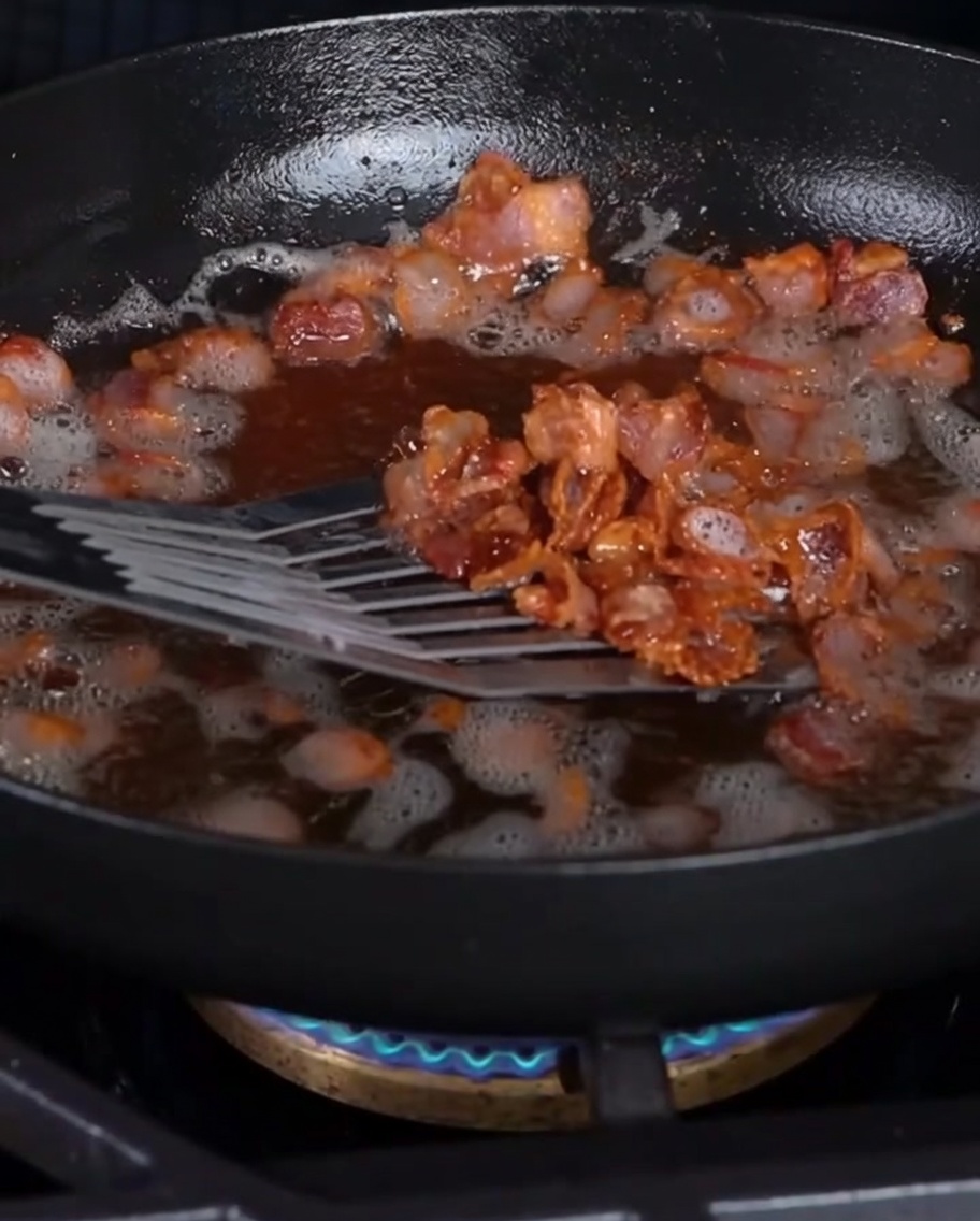 Crispy bacon bits being lifted from a pan with a slotted spatula.