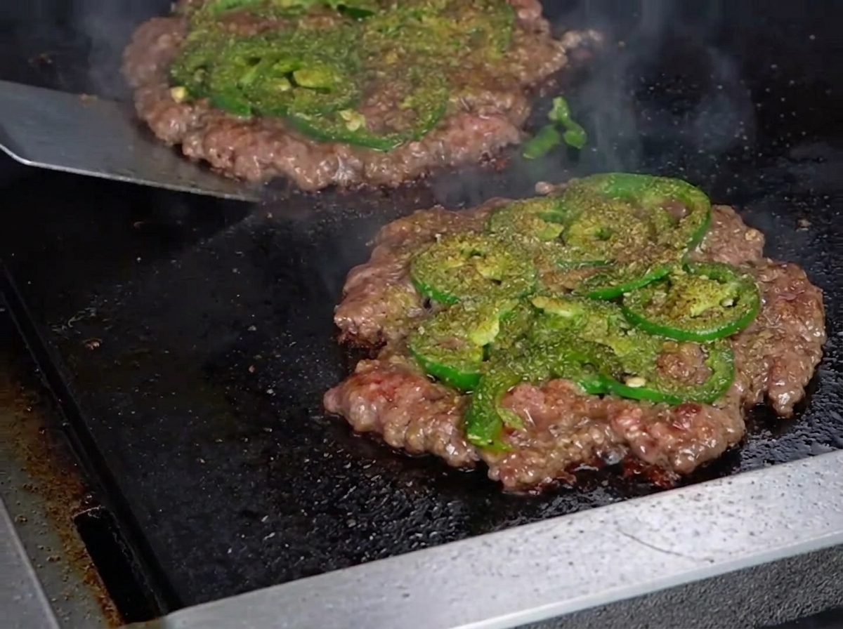 A metal spatula flipping a thin smashburger patty, revealing a perfectly browned, crispy crust on the bottom side.