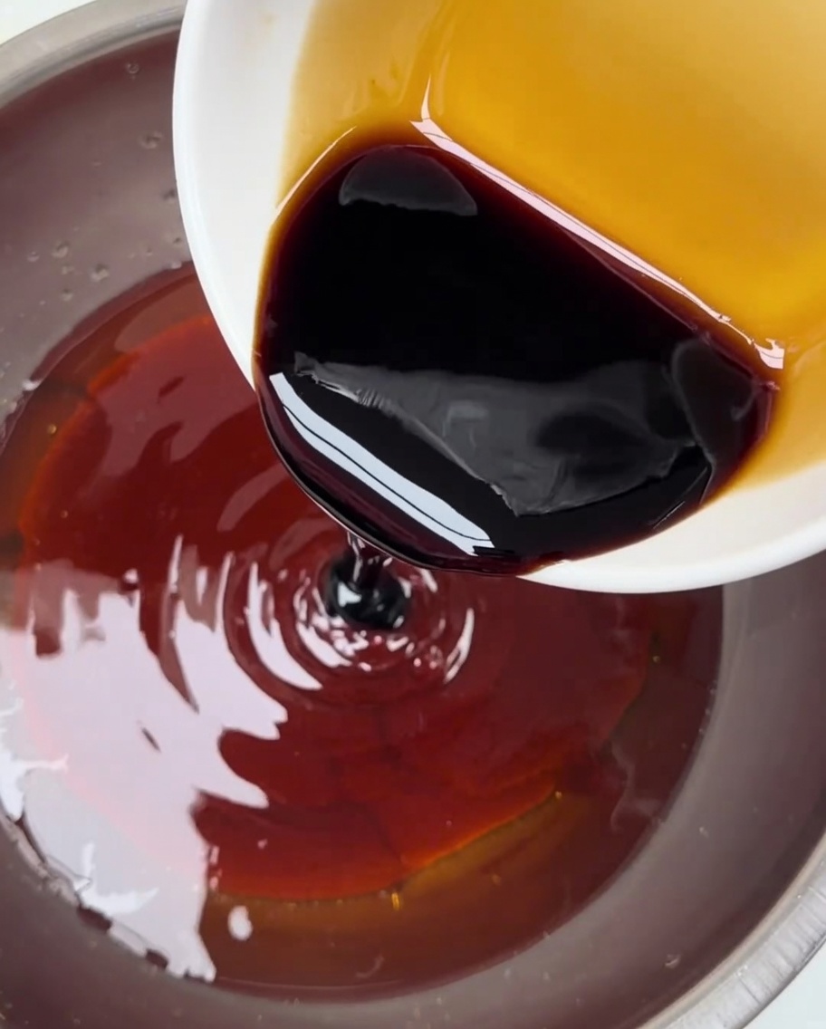 Dark soy sauce being poured from a small bowl into a larger container holding the red chili paste mixture.