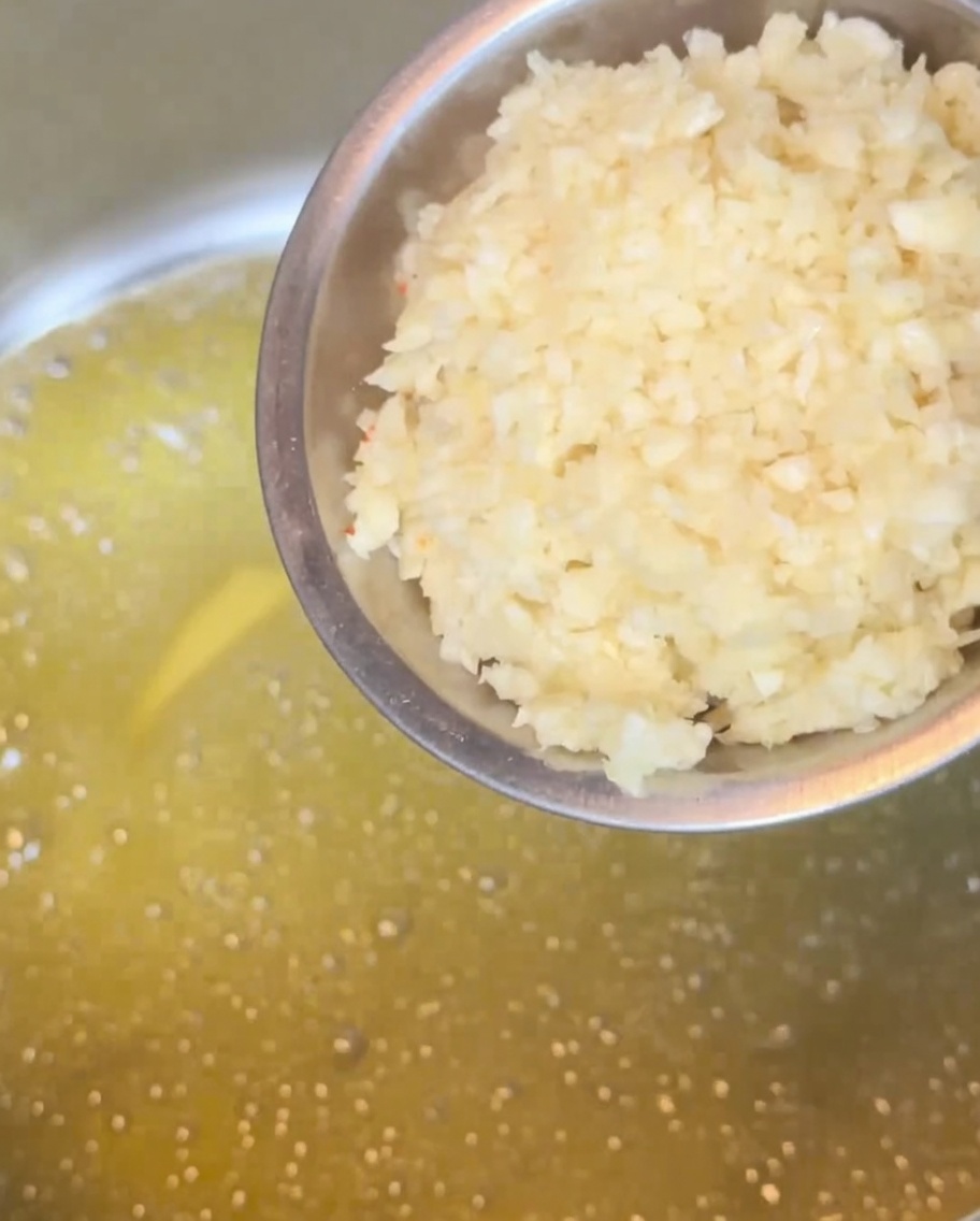 Minced garlic frying in a pool of melted butter in a metal pot, turning golden brown.