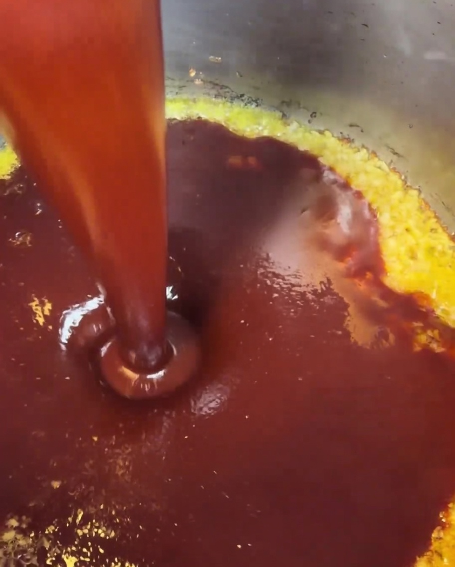 The blended red sauce being poured into a pot where minced garlic and butter are already simmering.