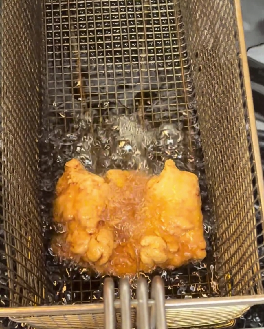 A single, golden-brown fried chicken thigh resting on a wire cooling rack.