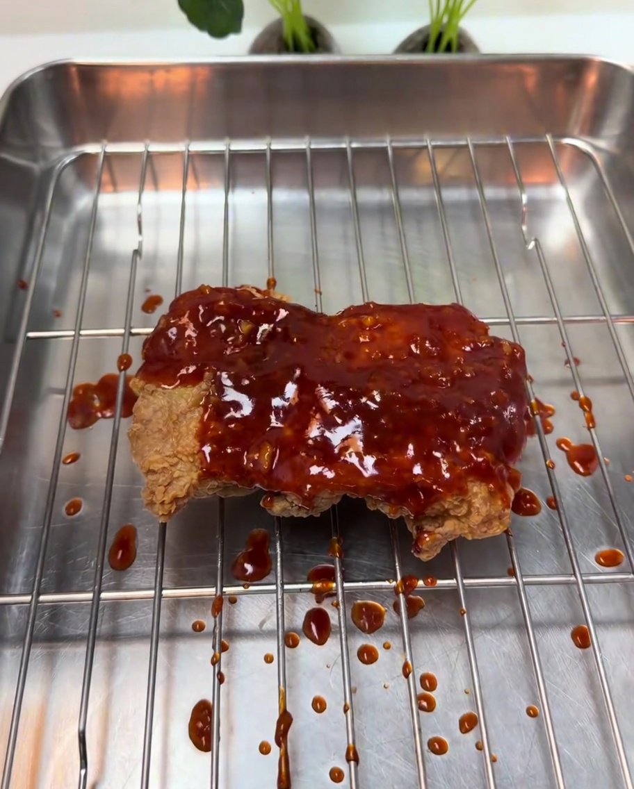 Thick, bubbling red chili glaze being poured over crispy fried chicken.