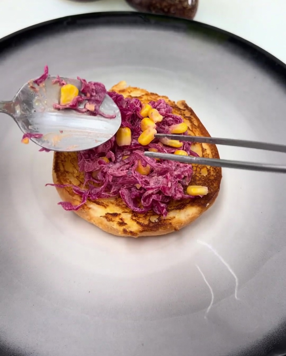 A glistening, sauce-coated fried chicken thigh resting on top of the purple cabbage slaw on the burger bun.