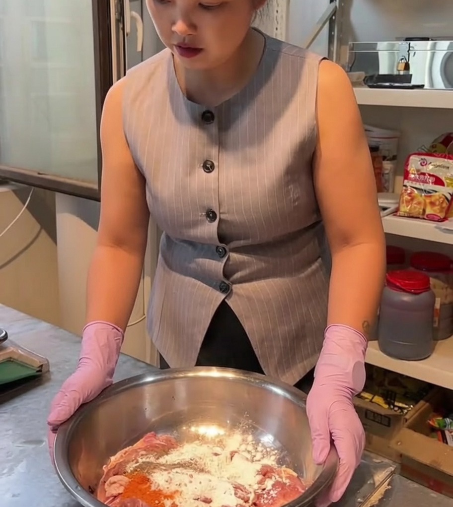 Raw chicken pieces being mixed with spices and marinade in a large stainless steel mixing bowl.