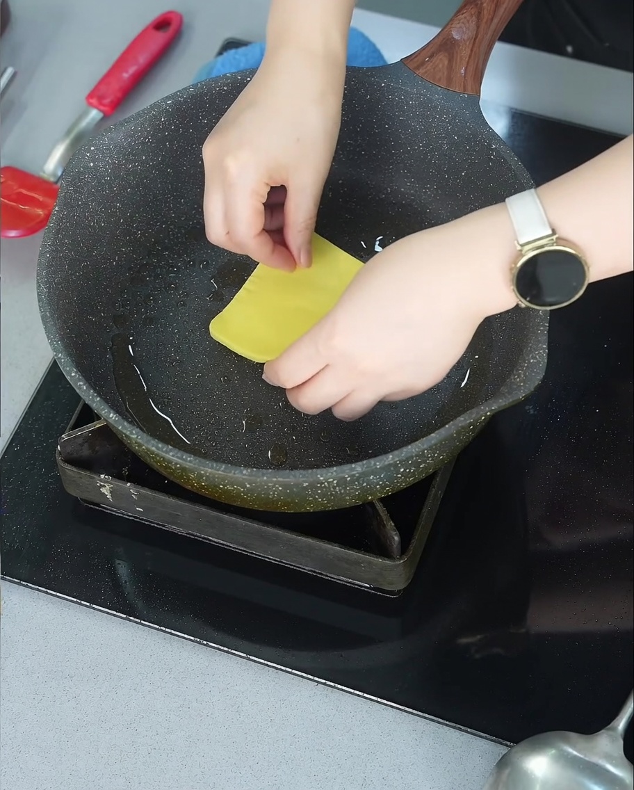 A slice of yellow cheese beginning to melt over a browned beef patty in a frying pan.