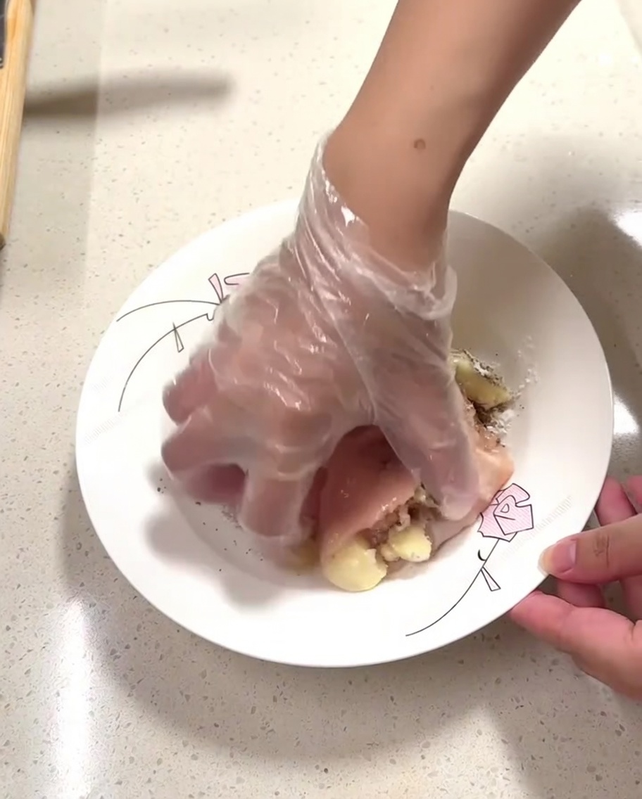A gloved hand massaging seasonings into raw chicken pieces on a plate.