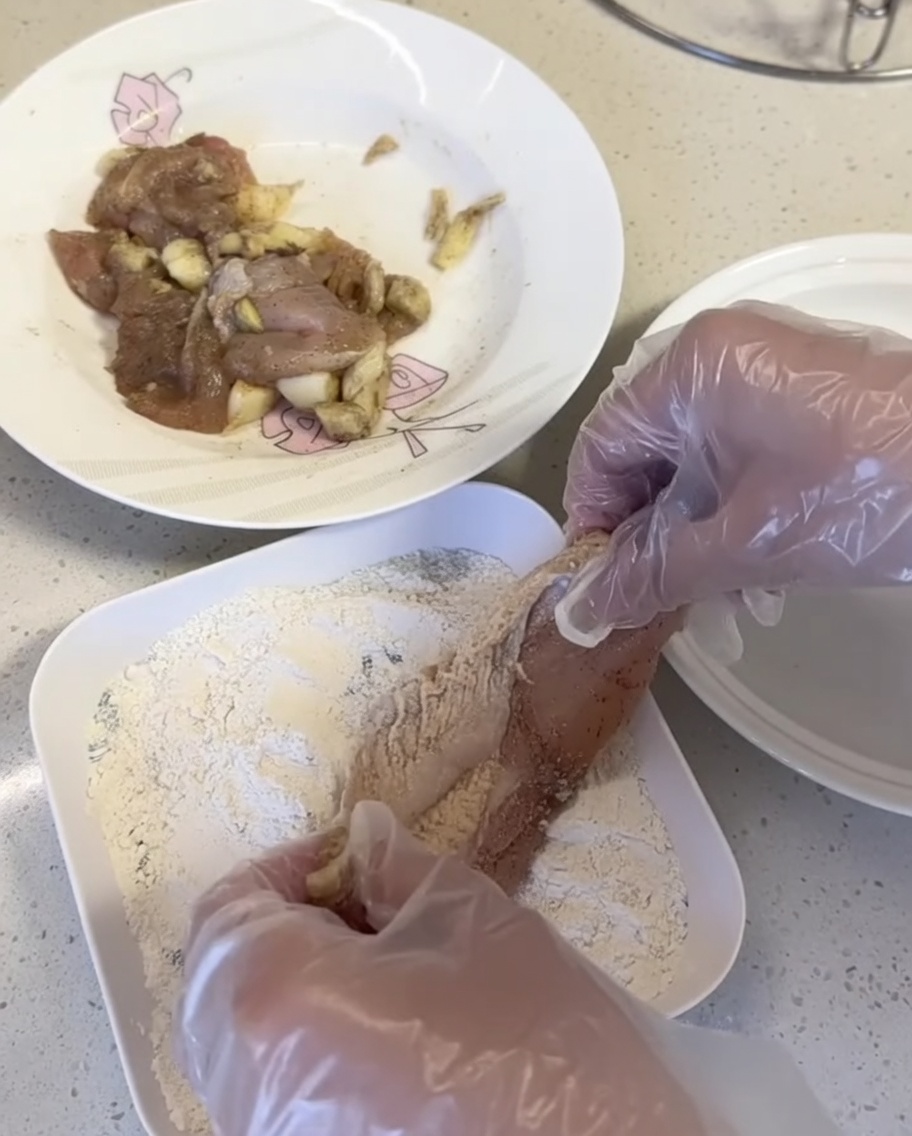 Chicken pieces being pressed into breading mix on a white plate.
